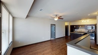 This single-floor unit offers a cohesive, open-concept design that seamlessly connects the living and kitchen areas. Dark hardwood-style flooring runs throughout the main living spaces, providing a warm contrast to the neutral-toned walls. Ceiling fans are present throughout, ensuring year-round comfort.

The kitchen is a standout feature, equipped with rich dark cabinetry, granite countertops, and a full suite of stainless steel appliances including a refrigerator, range, and microwave. A large central island with matching granite provides additional prep space and casual seating. Pendant lighting above the island and a decorative wine rack add refined touches. The kitchen flows naturally into the main living area, which benefits from a ceiling fan and access to an adjacent room.

A secondary living or flex space features large windows that invite natural light and provide exterior views, along with a ceiling fan and continued hardwood-style flooring.

The bedrooms are finished with plush carpeting, ceiling fans, and ample natural light from well-sized windows. Multiple doorways suggest convenient access to closets and adjoining spaces.

The bathroom features a clean, white tub and shower combination with built-in shelving, complemented by neutral walls and dark hardwood-style flooring.