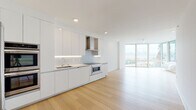 Located at 7401 River Rd in North Bergen, NJ, this contemporary residence delivers a clean, modern aesthetic throughout its single-floor layout. Wide-plank light hardwood flooring flows seamlessly across the open living and kitchen areas, complemented by crisp white walls and recessed lighting that create a bright, airy atmosphere.

The kitchen is a standout feature, showcasing high-gloss white cabinetry extending to the ceiling, under-cabinet LED lighting, a glass tile backsplash, and a suite of stainless steel appliances including a double wall oven, built-in microwave, induction cooktop, and a stainless range hood. The open-plan layout connects the kitchen directly to the living area, which is anchored by expansive floor-to-ceiling windows offering impressive views of the New York City skyline.

The bedrooms are generously proportioned, filled with natural light through large windows framing striking views of natural rock formations and lush greenery. Ceiling fans add practical comfort to each room. A walk-in closet features custom dark wood shelving with integrated drawers for ample storage.

The bathrooms are finished with large-format travertine-style tiles, warm wood-toned vanities, illuminated mirrors, and modern chrome fixtures. The primary bathroom includes a spacious glass-enclosed walk-in shower with a rainfall showerhead, delivering a spa-like experience.