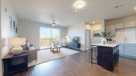 This single-floor residence presents a thoughtfully designed open-concept layout that seamlessly connects the main living areas. The living room is bright and welcoming, featuring wood-style flooring, a ceiling fan, and a large sliding glass door that opens onto a private balcony, offering expansive outdoor views of the surrounding landscape. The balcony provides an ideal vantage point to enjoy the scenery.

The kitchen is well-equipped with stainless steel appliances, light gray cabinetry paired with a contrasting dark-toned island, white countertops, and a clean tile backsplash. The island includes bar seating, creating a practical space for casual dining or entertaining. Wood-style flooring continues throughout the kitchen and living areas, contributing to a cohesive aesthetic.

The primary bedroom is generously sized, featuring plush carpet, a ceiling fan, and wide windows that invite natural light while framing outdoor views. A spacious walk-in closet with wire shelving provides ample storage. The attached bathroom includes a dual-sink vanity with white countertops, gray cabinetry, and a large mirror.

The secondary bedroom also features carpet flooring, a broad window with scenic views, and comfortable proportions, making it a versatile space suitable for guests or a home office.
