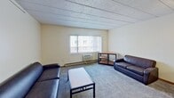 Located at 646 East College Avenue in State College, PA, this 3-bedroom, 2-bathroom apartment spans 840 square feet across a single floor. The combined kitchen and living area serves as the central hub of the unit. The kitchen features granite-style countertops, light wood cabinetry, black appliances including a refrigerator, electric range, and dishwasher, a stainless steel sink, and hardwood-style flooring. A breakfast bar with bar stools connects the kitchen to the living space, which is carpeted and includes windows with vertical blinds providing natural light. The living room comfortably accommodates seating and a coffee table. Two of the bedrooms are configured as double-occupancy rooms, each featuring two lofted beds with built-in dresser storage, individual desks, and chairs, along with windows and carpet flooring. The primary bedroom, at 230 square feet, is set up for single occupancy. The two bathrooms include one with a glass-enclosed shower stall and one with a shower-tub combination, each equipped with a vanity and mirror. Hallways connect the rooms efficiently throughout the unit, and a closet provides additional storage.