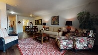This two-floor residence offers a well-organized and functional layout with a warm, inviting ambiance throughout. The main level is anchored by a comfortable living room featuring hardwood-style flooring, a textured ceiling, and large sliding glass doors fitted with vertical blinds that flood the space with natural light and provide access to a private outdoor patio with exterior views. Adjacent to the living room, the dining area accommodates a full-sized dining table and flows seamlessly into the kitchen. The kitchen is outfitted with warm oak cabinetry, laminate countertops, a double sink beneath a window, and includes a dishwasher, electric range, and an in-unit washer. A hallway on the main level features hardwood-style flooring and textured ceilings, with access to additional rooms. A half bathroom with wainscoting detail and hardwood-style flooring is also present on this level. The staircase leads to the upper floor, where a generously sized bedroom offers plush carpeting, natural light from a window with blinds, and ample space. The textured ceilings continue throughout both levels, contributing to the cohesive aesthetic of the home.