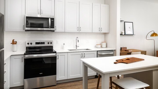 Cocina Design Collection II con electrodomésticos de acero inoxidable, gabinetes grises, salpicadero de azulejos blancos, encimeras de cuarzo blanco y pisos de superficie dura (foto representativa) - Avalon Quincy Adams