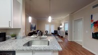 This single-floor residence offers a thoughtfully designed open-concept layout that seamlessly connects the kitchen, dining, and living areas. The kitchen is well-equipped with granite countertops, white cabinetry, black appliances including a refrigerator, range, microwave, and dishwasher, alongside a large undermount sink set into a peninsula that overlooks the main living space. The dining area accommodates a full table and chairs, while hardwood flooring flows throughout the main living areas, adding warmth and cohesion to the space.

The living room is highlighted by crown molding, a ceiling fan, and French doors that allow natural light to fill the room and provide access to the exterior. The bedroom is generously sized with plush carpeting, a ceiling fan, and a large window that brings in additional natural light. It connects directly to a full bathroom featuring granite countertops, white cabinetry, tile flooring, and a well-lit vanity mirror. Adjacent to the bathroom is a carpeted walk-in closet with wire shelving, offering ample storage. The neutral color palette and consistent finishes throughout the home create a cohesive, comfortable living environment.
