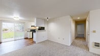 This single-story home offers five bedrooms, two bathrooms, and a thoughtfully arranged floor plan designed to maximize functionality. The open-concept living and kitchen area serves as the heart of the home, where wood-look flooring transitions into soft carpeting in the living space. The kitchen features white cabinetry, black appliances including an electric range and refrigerator, and a breakfast bar-style peninsula. A large sliding glass door floods the living area with natural light and provides views of the outdoors, creating a bright and welcoming atmosphere. The five bedrooms are carpeted and finished with clean white walls, offering a neutral and versatile canvas. The primary bedroom is a comfortable size and includes access to a dedicated walk-in closet equipped with extensive wire shelving on multiple walls and a full-length mirror. The bathrooms are functionally appointed, with at least one featuring a full tub-shower combo with chrome fixtures and wood-look flooring. A hallway connects the bedrooms and common areas, contributing to an efficient layout. Throughout the home, the design is clean and understated, emphasizing practicality and ease of use.
