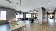 Located at 1971 Willow Loop Way in Knoxville, Tennessee, this single-floor space showcases a refined, open-concept design that effortlessly blends style and functionality. The layout flows seamlessly from the kitchen through the living and dining areas, creating a cohesive and inviting environment throughout.

The kitchen is appointed with granite or stone-look countertops and a double-basin sink, complemented by a striking row of industrial-style pendant lights that hang from the ceiling, adding a bold design statement. The light wood-toned flooring extends throughout the space, providing warmth and visual continuity.

The living area is anchored by a comfortable seating arrangement featuring upholstered chairs and a glass-top coffee table, set atop an area rug that defines the zone. Decorative columns with paneled detailing add architectural character and help delineate spaces without interrupting the open feel.

A coffered ceiling with recessed lighting elevates the dining area, lending it a sense of grandeur and refinement. Large windows along the perimeter allow abundant natural light to fill the space, while drapery panels add softness to the overall aesthetic. Neutral gray tones on the walls harmonize with the modern furnishings, creating a polished and welcoming ambiance throughout.