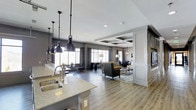 Located at 1971 Willow Loop Way in Knoxville, Tennessee, this single-floor space showcases a refined, open-concept design that effortlessly blends style and functionality. The layout flows seamlessly from the kitchen through the living and dining areas, creating a cohesive and inviting environment throughout.

The kitchen is appointed with granite or stone-look countertops and a double-basin sink, complemented by a striking row of industrial-style pendant lights that hang from the ceiling, adding a bold design statement. The light wood-toned flooring extends throughout the space, providing warmth and visual continuity.

The living area is anchored by a comfortable seating arrangement featuring upholstered chairs and a glass-top coffee table, set atop an area rug that defines the zone. Decorative columns with paneled detailing add architectural character and help delineate spaces without interrupting the open feel.

A coffered ceiling with recessed lighting elevates the dining area, lending it a sense of grandeur and refinement. Large windows along the perimeter allow abundant natural light to fill the space, while drapery panels add softness to the overall aesthetic. Neutral gray tones on the walls harmonize with the modern furnishings, creating a polished and welcoming ambiance throughout.