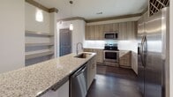 Located along Ronald Reagan Boulevard in Alpharetta, Georgia, this single-floor residence offers a well-designed layout with contemporary finishes throughout. The open-concept living and dining area features dark hardwood-style flooring, crown molding, and recessed lighting, creating a clean and cohesive aesthetic that flows seamlessly into the kitchen.

The kitchen is a standout feature, appointed with warm wood-toned cabinetry, granite countertops, a marble-look tile backsplash, and a full suite of stainless steel appliances including a range, microwave, and French door refrigerator. A built-in wine rack adds a refined touch, while pendant lighting and an island with a stainless steel sink enhance both form and function.

The bedrooms are generously sized with large windows that invite natural light and offer views of the surrounding greenery. Ceiling fans provide added comfort, and the rooms include closets with built-in shelving for organized storage.

The bathrooms are thoughtfully finished with granite-topped vanities, wood-toned cabinetry, and tile surround. One bathroom features a glass-enclosed walk-in shower, while the other includes a full soaking tub. Dark hardwood-style flooring runs consistently throughout the space, unifying the overall design with a modern, upscale character.