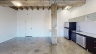 Located on Beverly Boulevard in Los Angeles, this single-floor space showcases a compelling industrial aesthetic that blends raw architectural elements with modern finishes. The open main area is defined by striking exposed wood beam ceilings supported by original structural columns, lending the space a loft-like character with generous vertical volume. Polished and raw concrete floors run throughout, adding to the industrial ambiance while providing a durable, easy-to-maintain surface.

The kitchen is well-appointed and runs along one wall, featuring dark cabinetry contrasted by a crisp white subway tile backsplash and light countertops. Upper cabinets with frosted glass-front doors add a contemporary touch, while stainless steel appliances — including a gas range, dishwasher, and refrigerator — complete the functional layout.

The remaining rooms offer bright, white-walled interiors with concrete floors and windows fitted with horizontal blinds that allow natural light to filter in. A separate room with a smoother ceiling finish provides a quieter, more enclosed feel compared to the open main area. The bathroom is clean and straightforward, equipped with a pedestal sink, toilet, and wall mirror. Overall, the space presents a versatile industrial character well-suited for a variety of uses.