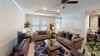 This single-floor residence offers a well-organized layout that connects key living spaces efficiently. The living room serves as the central gathering area, distinguished by a tray ceiling with crown molding detailing and a ceiling fan with recessed lighting. Multiple windows fitted with horizontal blinds allow natural light to fill the room, while light hardwood-style flooring runs throughout the common areas.

The kitchen is thoughtfully designed with rich, dark espresso cabinetry extending to the ceiling, providing generous storage capacity. Stainless steel appliances include a range, over-the-range microwave, and a full-size refrigerator, complemented by white countertops and a classic subway tile backsplash. A dedicated built-in desk area adjacent to the kitchen offers a functional workspace.

Both bedrooms feature ceiling fans, carpeted flooring, and windows that allow natural light, providing comfortable and private retreats. Each room accommodates standard bedroom furnishings with ease.

The bathroom is accessed via a narrow hallway and includes a shower-tub combination with a decorative curtain, light hardwood-style flooring, and practical storage solutions. The overall color palette throughout the residence remains neutral and light, contributing to a cohesive and welcoming ambiance.