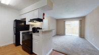 This single-floor, 2-bedroom, 1-bathroom unit is thoughtfully laid out to maximize functionality and comfort. The living area features neutral-toned walls and soft carpeting, creating a warm and inviting atmosphere. A large sliding glass door dressed with vertical blinds allows natural light to fill the space while providing access to the outdoors. The kitchen is designed for efficiency, featuring a galley-style layout with white cabinetry, light granite-style countertops, a double sink, and black appliances including a gas range, refrigerator, and dishwasher. A peninsula counter separates the kitchen from the living area, offering both additional prep space and an open connection to the main living space. Hardwood-style flooring runs through the kitchen and entry areas, transitioning to carpet in the living and sleeping spaces. Both bedrooms are comfortably sized with neutral carpeting and windows that bring in natural light. The full bathroom includes a combined tub and shower with clean white surrounds and hardwood-style flooring. Throughout the unit, clean white trim and understated finishes create a cohesive, move-in-ready environment suited for a range of living needs.