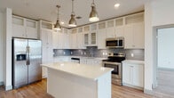 This well-designed single-floor residence offers a clean, contemporary aesthetic with thoughtful finishes throughout. The heart of the home is a striking kitchen outfitted with white shaker-style cabinetry extending to the ceiling with open display shelving above, a grey subway tile backsplash, stainless steel appliances including a French door refrigerator, range, microwave, and dishwasher, and a spacious central island with a bright white countertop. Industrial-style brushed gold pendant lights hang overhead, adding a refined touch to the space.

The kitchen flows seamlessly into an open living area, all united by warm hardwood-style flooring. The bedrooms are bright and airy, each featuring ceiling fans with light fixtures and large windows dressed with blinds that invite natural light. The primary bathroom is generously proportioned, offering a soaking tub with white subway tile surround, a vanity with white countertop, and direct access to a spacious walk-in closet complete with wire shelving and hanging storage. The secondary bathroom mirrors a similar clean design. A dedicated in-unit laundry room with a full-size washer and dryer rounds out the functional layout of this modern residence.
