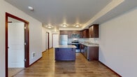 Located at 14500 51st Ave NE in Marysville, Washington, this well-appointed 2-bedroom, 1-bathroom unit offers a thoughtfully designed layout across a single floor. The kitchen serves as a standout feature, showcasing rich dark-wood cabinetry, granite-style countertops, a tile backsplash, stainless steel appliances including a refrigerator, range, microwave, and dishwasher, and a central island with additional storage. Warm wood-look plank flooring runs throughout the kitchen and living areas, lending a cohesive and contemporary feel. Both bedrooms are carpeted and receive natural light through windows with outdoor views of surrounding greenery. The primary bedroom includes direct access to a dedicated walk-in closet outfitted with wire shelving and hanging rods for ample storage. The bathroom is finished with a granite-topped vanity featuring dark wood cabinetry, and conveniently houses a stacked washer and dryer unit, integrating laundry within the home. Rich wood baseboards and trim provide a consistent design element throughout the space, complementing the neutral wall tones and creating a warm, welcoming ambiance overall.