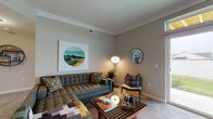 This well-appointed single-floor residence at 484 Greenmont Dr in Lewis Center, Ohio, offers a thoughtfully designed layout with modern finishes throughout. The kitchen is a standout feature, showcasing dark cabinetry with granite-style countertops, stainless steel appliances including a refrigerator, stove, and microwave, and a central island with pendant lighting and seating — all set atop durable wood-look flooring. The living area is generously sized, finished with plush carpeting, crown molding, and a large sliding glass door that fills the room with natural light and provides direct outdoor views. The primary bedroom is spacious with soft carpet, a ceiling fan, and a private en-suite bathroom featuring wood-look flooring, a dark vanity with granite countertops, and a shower-tub combination. A second bedroom offers comfortable proportions with closet access, while a second bathroom includes a glass-enclosed shower, dark cabinetry, and matching granite countertops. Neutral gray tones are carried consistently throughout the home, creating a cohesive and calming aesthetic. A connecting hallway with natural light from a bright window ties the spaces together seamlessly, enhancing the open and airy feel of this well-designed residence.
