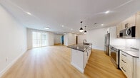 This well-designed 2-bedroom residence at 4101 Taylor Pond Ln in Billerica, Massachusetts offers a thoughtfully planned single-level layout with modern finishes throughout. The open-concept kitchen and living area forms the heart of the home, centered around a striking kitchen island with a dark quartz countertop, an undermount sink, and stylish pendant lighting overhead. The kitchen is equipped with stainless steel appliances, including a full-size refrigerator, range, and built-in microwave, complemented by a combination of white and light wood cabinetry. Light hardwood flooring runs seamlessly throughout the entire residence, creating a warm and cohesive aesthetic. The living area is bright and open, benefiting from a large sliding glass door that invites natural light and provides outdoor views of the surrounding greenery. Both bedrooms are well-proportioned, with the primary bedroom offering ample space. Each room features clean white walls, recessed lighting, and the same consistent hardwood flooring. Mini-split HVAC units are installed for efficient climate control. Shaker-style interior doors in a muted gray tone add a refined, contemporary touch throughout the space, completing the home's modern and functional character.