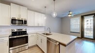 This single-floor residence offers a thoughtfully designed layout with contemporary finishes throughout. The kitchen serves as a central highlight, showcasing white shaker-style cabinetry, stainless steel appliances including a French door refrigerator, electric range, built-in microwave, and dishwasher. A peninsula with a stone-look countertop provides additional workspace and casual seating, while pendant lighting with globe fixtures adds a modern touch. Light hardwood flooring runs throughout the main living areas, complementing the neutral gray tones of the walls.

A dedicated mudroom near the entry features built-in bench seating, wall hooks, and paneled gray doors, offering a practical and organized transition space. The bedrooms are carpeted for comfort, each benefiting from natural light through sizable windows with blinds and ceiling fans. One bedroom includes built-in corner shelving, adding functional storage and character.

The bathroom is clean and well-equipped, featuring a dual-sink vanity with white cabinetry, stone-topped counters, framed mirrors, and a frameless glass walk-in shower. A spacious walk-in closet with multi-level wire shelving rounds out the storage offerings, completing this practical and modern living space.