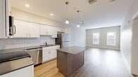 Located at 50 Bridge Street in Shelton, CT, this well-designed two-bedroom, one-bathroom residence offers a thoughtful, efficient layout across a single floor. The open-concept kitchen and living area serves as the heart of the home, featuring crisp white shaker-style cabinetry, a classic subway tile backsplash, dark quartz countertops, and a center island with additional storage. A full suite of stainless steel appliances — including a refrigerator, range, microwave, and dishwasher — completes the kitchen. Pendant lighting above the island adds a polished finishing touch, while recessed lighting illuminates the space evenly. The living area flows seamlessly from the kitchen, bathed in natural light from multiple windows. Light-toned hardwood flooring runs consistently throughout the entire residence, creating a cohesive and clean aesthetic. Both bedrooms are well-proportioned and bright, each offering natural light through slatted windows. The spacious primary bedroom includes a walk-in closet with wire shelving for ample storage. The full bathroom is clean and functional, featuring a white vanity with shaker-style cabinetry, a framed mirror, and a walk-in shower. Neutral gray walls throughout provide a versatile backdrop suited to a variety of interior styles.