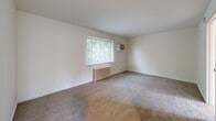 Located at 3815 Brotherton Rd in Cincinnati, Ohio, this single-floor unit offers a straightforward and functional layout with a clean, neutral aesthetic throughout. The spacious main living area is finished with wall-to-wall carpet and features a large window dressed with blinds that frames lush greenery, allowing generous natural light to fill the room. A classic cast-iron radiator and a wall-mounted air conditioning unit ensure year-round comfort. The bedroom continues the carpeted flooring and includes a ceiling fan with light fixture, a closet, and additional windows that bring in soft, diffused light. The kitchen is well-equipped with granite-style countertops, white cabinetry, a gas range, a dishwasher, and a stainless steel sink. A window above the counter provides natural light and neighborhood views. The flooring in the kitchen features a stone-look tile pattern that extends into the bathroom. The bathroom is neatly appointed with full tile surround in the tub and shower area, a pedestal sink, a mirrored medicine cabinet with overhead storage, and a ceiling fan. Throughout the unit, the white walls and neutral finishes create a bright, clean environment that is move-in ready.