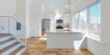 This contemporary two-floor residence offers a thoughtfully designed layout that blends modern finishes with functional living spaces. The main level features an open-concept living and dining area bathed in natural light, with warm hardwood flooring that flows seamlessly throughout. Soaring ceilings lend a sense of grandeur to the space, while large windows and glass patio doors frame expansive urban views and invite abundant sunlight indoors. The kitchen is a standout, anchored by a generous central island with a granite countertop, white shaker cabinetry, stainless steel appliances, and elegant pendant lighting overhead. A staircase connects the two levels with clean, contemporary detailing. The upper floor hosts well-proportioned bedrooms, each featuring hardwood floors, bright windows with city views, and ample closet space — including a walk-in closet with built-in hanging rods. Two full bathrooms serve the residence, both finished with large-format tile flooring and clean white fixtures. One bathroom offers a tub-shower combination, while the other features a glass-enclosed shower. Clean white walls, crisp trim, and modern chrome fixtures throughout create a cohesive, move-in-ready aesthetic that is both understated and refined.