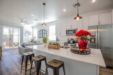 This two-story home showcases a clean, contemporary design with a bright, neutral color palette carried consistently throughout. The main level centers around an open-concept layout where the kitchen flows seamlessly into the living area. The kitchen is well-appointed with white shaker-style cabinetry, quartz countertops, stainless steel appliances including a French door refrigerator, electric range, and built-in microwave. A spacious island with seating provides an ideal casual dining spot, illuminated by pendant lighting overhead. Light wood-look flooring runs throughout the main living areas, enhancing the airy feel.

The living room features a ceiling fan, large windows, and sliding glass door access to a private outdoor patio, filling the space with natural light. A convenient half bath is located on the main level. A dedicated laundry room houses full-size side-by-side washer and dryer units with overhead shelving.

Upstairs, the bedrooms feature plush carpeting, ceiling fans, and generous windows. The primary bedroom includes an en-suite bathroom, while additional bedrooms are served by a full bathroom complete with a tub-shower combination, white vanity, and wood-look flooring.