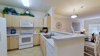 This single-floor residence offers a thoughtfully designed layout encompassing two bedrooms, two bathrooms, a combined living and dining area, a full kitchen, a hallway, and a closet. The open-concept living room is bright and airy, featuring vaulted ceilings, large windows with horizontal blinds that invite natural light, crown molding, and soft carpeting throughout. It flows seamlessly into the dining area, which is defined by a pendant light fixture and connects directly to the kitchen.

The kitchen is well-equipped with light wood cabinetry, white appliances including a range, built-in microwave, dishwasher, and refrigerator, along with tile flooring and a peninsula countertop that opens toward the dining space—ideal for casual interaction.

The primary bedroom offers a generous footprint with vaulted ceilings, a ceiling fan, a large window, and plush carpeting, accompanied by a private closet. The second bedroom is similarly carpeted and bright, with a window and closet access. Both bathrooms are finished with tile flooring, white vanity cabinetry, and shower/tub combinations, maintaining a clean and functional aesthetic throughout. The overall ambiance is warm and neutral, with a cohesive palette of soft creams and beiges across every room.