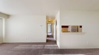 This single-floor unit in Fort Gratiot, Michigan, offers a practical and well-organized layout designed to maximize comfort and functionality. The living area is generously sized, featuring plush wall-to-wall carpeting and a large window dressed with vertical blinds that allows abundant natural light to fill the space. A pass-through counter connects the living area to the kitchen, which is equipped with dark wood cabinetry, a light-colored countertop, and a refrigerator, providing a convenient and efficient workspace.

A carpeted hallway extends from the main living area, leading to the two bedrooms and the shared bathroom. Both bedrooms are well-proportioned, carpeted, and brightened by windows with vertical blinds. Each room includes closet storage with louvered bifold doors, offering organized storage space. One bedroom features multiple closets, adding to its practicality.

The bathroom is finished with light ceramic tile flooring, a rich wood-toned vanity with an integrated sink, a large mirror with overhead lighting, and a separate toilet area. The unit's neutral color palette, consistent carpeting, and clean finishes throughout contribute to a cohesive and move-in-ready living environment.