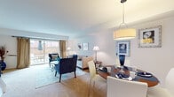 This two-floor residence offers a thoughtfully designed layout that balances comfort and functionality across its living spaces. The main level opens into a combined living and dining area bathed in natural light from large sliding glass doors that lead to a private outdoor patio. The living room features plush carpeting, a tufted sofa accented with bold navy cushions, and coordinating velvet armchairs arranged around a glass-top coffee table, creating a welcoming and cohesive aesthetic. A pendant light anchors the adjacent dining area, where a round wood table and contemporary chairs provide an intimate setting for meals.

The kitchen is equipped with warm wood cabinetry, light stone countertops, a tile backsplash, and stainless steel appliances including a gas range and refrigerator, offering ample storage and prep space. Tile flooring completes the practical yet attractive finish.

The bedrooms are carpeted and generously sized, each featuring wide windows that invite natural light and outdoor views. The primary bedroom accommodates a full dresser, seating area, and dual nightstands. A secondary bedroom offers similar proportions and charm. The bathroom includes a tiled tub-shower combination, vanity with under-sink storage, and tile flooring.