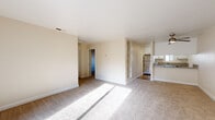 Located at 4001 S Watt Ave in Sacramento, CA, this single-floor unit offers six bedrooms and two full bathrooms across a well-organized layout. The open living room features neutral carpet, a ceiling fan, and a tiled fireplace, creating a comfortable communal space. Adjacent to the living area, the kitchen is equipped with stainless steel appliances — including a range, microwave, dishwasher, and refrigerator — complemented by granite countertops, a stainless steel sink, and crisp white cabinetry over wood-look flooring. Built-in shelving near the kitchen provides additional storage and display space. The bedrooms are carpeted throughout, with warm neutral tones and ample natural light from large windows offering leafy outdoor views. The primary bedroom features sliding glass doors that open to a private balcony. A walk-in closet with wrap-around hanging rods offers generous storage capacity. Both bathrooms are finished with granite-topped vanities, white cabinetry, large mirrors, and wood-look flooring, with one featuring a shower-tub combo and a natural light window. The overall aesthetic is clean and functional, with a consistent warm, neutral palette throughout.
