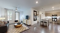This single-story residence is designed with a contemporary open-concept layout that seamlessly connects the living, dining, and kitchen areas. Dark hardwood-style flooring runs throughout, providing a warm contrast to the crisp white walls and creating a cohesive flow between spaces.

The kitchen is a standout feature, outfitted with light wood grain cabinetry, granite countertops, a full suite of stainless steel appliances, and a tiled backsplash. A central island with seating offers additional prep space and casual dining. Pendant lighting and under-cabinet illumination enhance the kitchen's functionality and ambiance. A built-in wine rack adds a refined touch above the cabinetry.

The living area is bright and comfortable, benefiting from natural light through large windows and a ceiling fan overhead. Built-in shelving provides display and storage space adjacent to the living room.

Two bedrooms each offer a relaxed retreat. The primary bedroom connects directly to an en-suite bathroom featuring a glass-enclosed shower, granite vanity, and gray cabinetry. The secondary bedroom includes an open closet area and generous window views. Both bedrooms are finished with ceiling fans and hardwood-style flooring.