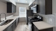 This efficient 420-square-foot single-floor unit is thoughtfully laid out to maximize functionality within a compact footprint. The space includes one bedroom and one kitchen, offering a straightforward and practical living arrangement.

The galley-style kitchen is a standout feature, designed with dark gray shaker cabinetry lining both walls, light quartz countertops, and a subtle tile backsplash. It is equipped with stainless and black appliances, including a refrigerator, electric range, and an over-the-range microwave. Light wood-look flooring runs throughout the kitchen, and a window fitted with horizontal blinds allows natural light to brighten the space.

The bedroom spans 140 square feet and features wall-to-wall carpet in a neutral brown tone, providing a warm and comfortable feel underfoot. Recessed lighting and a window with blinds offer both ambient illumination and natural light. A ceiling fan with an integrated light fixture is also present, contributing to year-round comfort and air circulation. The room's neutral white walls create a clean, versatile backdrop.

Overall, the unit maintains a neutral, modern aesthetic with white walls throughout, carpet in living areas, and consistent finishes that give the space a cohesive and well-maintained appearance.