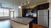 This single-story residence showcases a thoughtfully designed open-concept layout where the kitchen flows seamlessly into the living area. The kitchen is a standout feature, equipped with rich dark cabinetry extending to the ceiling, granite countertops, and a full suite of stainless steel appliances including a refrigerator, range, and over-the-range microwave. A curved island with an undermount sink and pendant lighting serves as a functional centerpiece, complemented by track lighting and a white tile backsplash. Crown molding adds a refined architectural detail throughout.

The living area is generously sized, featuring warm hardwood-style flooring, crown molding, and a ceiling fan for added comfort. Natural light enters through window treatments, enhancing the open feel of the space.

Bedrooms include both hardwood-style and carpeted flooring options. One bedroom features an arched window, while another includes a ceiling fan. A walk-in closet with built-in shelving and hanging rods provides organized storage. The bathroom is finished with matching dark cabinetry, granite countertops, tile flooring, a soaking tub, and direct access to the walk-in closet, creating a cohesive and practical layout throughout.