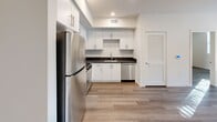 Located at 10555 S Bloomfield St in Los Angeles, CA, this single-floor unit offers a clean, modern aesthetic throughout. The open-concept layout connects the living area to the kitchen, creating a spacious and functional flow. Warm hardwood-style flooring runs continuously across the entire unit, complementing the crisp white walls and recessed lighting.

The kitchen is well-appointed with white shaker-style cabinetry, dark countertops, a stainless steel refrigerator, dishwasher, and a gas range. A convenient in-unit stacked washer and dryer is integrated seamlessly into the kitchen area, adding everyday practicality.

The bedroom features large windows that invite abundant natural light and offer pleasant views of the surrounding greenery. A mirrored sliding closet door enhances the sense of space while providing ample storage. An additional room offers versatile use as a bedroom or office, also benefiting from natural light.

Sliding glass doors lead to a private balcony, providing an outdoor retreat with elevated views of the neighborhood and mature trees. The unit's neutral palette, contemporary finishes, and thoughtful layout make it a bright and inviting space well-suited for modern living in Los Angeles.