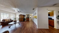 This single-floor home offers a thoughtfully designed layout that balances open living spaces with functional, private areas. Rich, dark hardwood flooring flows throughout the main living areas, creating a warm and cohesive aesthetic. The spacious living room serves as a central gathering point, anchored by a classic brick fireplace and framed by large windows that invite natural light and outdoor views. A ceiling fan overhead adds comfort to the room's inviting atmosphere. Adjacent to the living room, a dedicated dining area provides an intimate setting, complete with a window that fills the space with additional natural light. The galley-style kitchen is efficiently arranged with dark granite-style countertops, warm wood cabinetry, and black appliances, offering ample storage and workspace. A built-in bar ledge along one wall adds a distinctive touch to the open corridor connecting the main areas. The bedrooms are carpeted for comfort, each featuring ceiling fans and generous windows, including sliding glass door access to an outdoor area in the primary bedroom. A well-lit bathroom with wood cabinetry and dark countertops completes the layout. Textured ceilings are present throughout, adding architectural character to this cohesive and comfortable home.