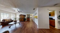 This single-floor home offers a thoughtfully designed layout that balances open living spaces with functional, private areas. Rich, dark hardwood flooring flows throughout the main living areas, creating a warm and cohesive aesthetic. The spacious living room serves as a central gathering point, anchored by a classic brick fireplace and framed by large windows that invite natural light and outdoor views. A ceiling fan overhead adds comfort to the room's inviting atmosphere. Adjacent to the living room, a dedicated dining area provides an intimate setting, complete with a window that fills the space with additional natural light. The galley-style kitchen is efficiently arranged with dark granite-style countertops, warm wood cabinetry, and black appliances, offering ample storage and workspace. A built-in bar ledge along one wall adds a distinctive touch to the open corridor connecting the main areas. The bedrooms are carpeted for comfort, each featuring ceiling fans and generous windows, including sliding glass door access to an outdoor area in the primary bedroom. A well-lit bathroom with wood cabinetry and dark countertops completes the layout. Textured ceilings are present throughout, adding architectural character to this cohesive and comfortable home.