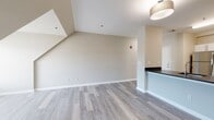 Located at 3 Schooner On in Milford, CT, this one-bedroom, one-bathroom residence offers a thoughtfully designed single-floor layout with contemporary finishes throughout. The open-concept living and dining area features light gray wood-look flooring, neutral warm-toned walls, and angled architectural ceiling details that add visual interest. A half-wall peninsula seamlessly connects the living space to the kitchen, which is outfitted with sleek white cabinetry, dark granite-style countertops, stainless steel appliances including a refrigerator, range, microwave, and dishwasher, and wood-look flooring that continues the cohesive aesthetic. The bedroom is generously sized with soft carpeting, a large window that brings in natural light with outdoor views of surrounding greenery, and a spacious walk-in closet with built-in shelving for ample storage. The bathroom is well-appointed with a vanity featuring dark countertops, a mirror, and a combination tub and shower enclosed by a sliding glass door, all set on matching wood-look flooring. The unit's consistent neutral palette and modern finishes create a clean, move-in-ready living environment suited for comfortable everyday living.