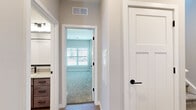 Located at 12101 Rockaway St in Ballston Spa, NY, this two-story home offers three bedrooms and three full bathrooms thoughtfully distributed across two floors. The main level hosts an open-concept kitchen and living area finished with light hardwood-style flooring. The kitchen is a standout feature, showcasing rich dark-stained cabinetry, a white subway tile backsplash, light quartz countertops, stainless steel appliances, and a peninsula with pendant lighting that provides both additional prep space and a casual dining area. An attached garage with a concrete floor and automatic door opener completes the ground level. Upstairs, the layout includes three well-proportioned bedrooms, each carpeted and filled with natural light from windows fitted with white blinds. The generously sized primary bedroom offers notable square footage. The bathrooms are finished to a modern standard, featuring light wood-style flooring, neutral-toned cabinetry with matte black hardware, undermount sinks, and a soaking tub with shiplap-style surround in the full bath. Hallways throughout are clean and bright with neutral paint tones and white panel doors, creating a cohesive and contemporary aesthetic across the entire home.
