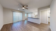 This single-story, 1-bedroom, 1-bathroom residence offers a thoughtfully laid-out floor plan that maximizes its compact footprint. The open-concept living and kitchen area serves as the heart of the home, featuring warm wood-look luxury vinyl plank flooring, neutral-toned walls, and ceiling fans with integrated lighting throughout. Large sliding glass doors dressed with vertical blinds flood the living room with natural light and provide access to the outdoors.

The kitchen is defined by a peninsula with a granite-style countertop, white cabinetry extending to the ceiling, pendant lighting, recessed lighting, and white appliances including a refrigerator, range, and microwave. The peninsula provides additional prep and seating space while maintaining visual connectivity to the living area.

The bedroom is a comfortable, well-proportioned room carpeted for warmth and comfort, featuring a ceiling fan, a natural light window with blinds, and a dedicated closet with built-in hanging rods for ample storage.

The bathroom is clean and modern, showcasing large white subway tile in the tub surround, a soaking tub, and a granite-accented vanity. Additional spaces include an entrance and a closet. The overall aesthetic is fresh and contemporary, with a cohesive, neutral palette throughout.
