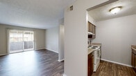 This single-story residence features a straightforward, functional layout with clearly defined living spaces. The living area is finished with dark wood-style flooring and neutral-toned walls, creating a clean, versatile backdrop. A sliding glass door with vertical blinds opens to a private balcony, allowing natural light to fill the space and providing an outdoor connection. A ceiling fan is positioned in the adjoining hallway area, adding both style and practicality.

The kitchen is designed in a galley configuration, featuring dark wood cabinetry, light countertops, a white electric range, and a stainless steel sink. Upper and lower cabinetry provide ample storage, while the wood-style flooring continues throughout, maintaining visual consistency.

The bedrooms are carpeted in a neutral tone, offering a comfortable and quiet atmosphere. Each room benefits from natural light, with one bedroom featuring a window with an exterior view. The bathroom is appointed with white cabinetry, a wide vanity with a large mirror, light countertops, and a tub-shower combination with tile surround. Textured ceilings are present throughout, adding a subtle architectural detail to the overall space.