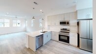 This three-floor home in California offers a well-organized layout across three distinct levels. The ground floor houses an attached garage with an automatic opener and concrete flooring, alongside a hallway entry featuring light wood-style flooring and a clean staircase with a wooden handrail connecting all levels.

The main living floor hosts a combined kitchen and living area. The kitchen is equipped with stainless steel appliances, including a French door refrigerator, electric range, and built-in microwave, complemented by light cabinetry and white countertops. The living area benefits from recessed lighting and a ceiling fan, with multiple windows allowing substantial natural light and neighborhood views.

The upper floor contains the three bedrooms and a shared full bathroom. Each bedroom features light wood-style flooring, crisp white walls, and windows providing natural light and outdoor views. The primary bedroom is notably well-lit, with corner windows. The bathroom includes a dual-sink vanity with white cabinetry, white quartz countertops, a large mirror, and two windows that enhance brightness throughout. Two closets provide additional storage within the home.