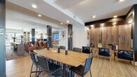 This thoughtfully designed single-floor community clubhouse offers a rich variety of functional zones, each with its own distinct character while maintaining a cohesive modern aesthetic throughout. The welcoming entrance lobby features large glass double doors that flood the space with natural light, complemented by light wood-look flooring, a contemporary chandelier, and an adjacent seating area for informal gatherings.

The main social hub centers around a large solid-wood communal dining table with woven leather chairs, set beneath recessed lighting and surrounded by dark accent columns. A reclaimed wood feature wall displays acoustic guitars, lending a creative, music-inspired energy to the space. Nearby, comfortable leather lounge seating and a flat-screen TV create a relaxed entertainment area.

A dedicated lounge corridor features built-in bench seating upholstered in neutral tones beneath a dramatic dark ceiling, ideal for intimate conversations. High-back booth seating with floor-to-ceiling windows provides semi-private nooks with outdoor views of the pool area, accessible via glass doors.

The amenity area includes a coffee and beverage station set against a bold Art Deco-patterned wallpaper, alongside a private office or leasing workspace with mosaic tile walls and reclaimed wood ceiling details. A business services counter with granite surfaces and a printer rounds out the practical offerings, making this clubhouse a well-appointed hub for community living.