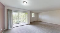 This single-floor residence offers a well-organized layout with a variety of functional spaces. The expansive living area is a standout feature, finished with neutral wall-to-wall carpeting and bathed in natural light from a large sliding glass door that opens onto a private balcony overlooking lush, mature greenery. A secondary window further brightens the space, creating an inviting and airy atmosphere.

The galley-style kitchen is efficiently designed with white cabinetry lining both sides, dark countertops, light tile flooring, and a full suite of black appliances including a range, refrigerator, and double-basin sink. A recessed ceiling with built-in lighting adds a practical touch to the workspace.

The unit includes multiple bedrooms, each carpeted in the same neutral tones as the living area and equipped with windows that allow for natural light. The rooms are clean and versatile, well-suited for a variety of uses.

Two bathrooms serve the unit. One features a wide dark-toned vanity countertop with an undermount sink, a large mirror, and tile flooring. The second is a more compact space with a walk-in shower stall, tile flooring, and a standard toilet. Both bathrooms maintain a clean, minimalist aesthetic throughout.
