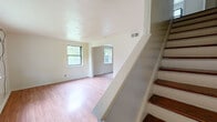 This two-story home at 236 Woodland Dr in Hartford, CT offers a practical and straightforward layout across two floors of nearly equal size. The main level features a bright front living room with multiple windows that invite natural light and views of the surrounding greenery. Light-toned laminate flooring runs throughout the main level, giving the space a clean, cohesive feel. A staircase connects the two floors, with a second living area on the main level providing additional flexible space. The kitchen is equipped with warm wood cabinetry, granite-patterned countertops, a subway tile backsplash, and dark slate tile flooring, offering ample counter and storage space. Upstairs, rich hardwood floors extend throughout both bedrooms. The spacious primary bedroom features two windows on opposing walls, filling the room with natural light. The second bedroom also includes a window with garden views and closet access. The full bathroom is finished with classic white subway tile, black accent tile trim, a tub-shower combination, and a window for natural ventilation. Overall, the home presents a functional, no-frills layout with consistent finishes throughout.