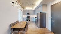 This three-bedroom, one-bathroom unit at 4720 Third Ave offers a thoughtfully designed layout that maximizes its compact footprint. Throughout the space, light wood flooring and crisp white walls create a clean, contemporary aesthetic, while exposed concrete ceilings add an industrial character that distinguishes the unit architecturally.

The open kitchen and dining area form the heart of the unit. The kitchen features grey flat-front cabinetry with under-cabinet lighting, stainless steel appliances including a refrigerator, microwave, and range, and a wood dining table with upholstered seating. Industrial-style pendant lighting and exposed ceiling details reinforce the modern-industrial design language.

Each of the three bedrooms features white walls, light wood flooring, and a window offering city views. The bedrooms include built-in wardrobes with wood-accented handles and dedicated desk areas, providing functional storage and workspace. The exposed concrete ceiling is a consistent design element across all bedrooms.

The bathroom is a standout feature, finished with floor-to-ceiling marble-patterned wall tiles, matte black fixtures, a soaking tub with a glass enclosure, a grey vanity, and warm wood flooring — delivering a refined, upscale feel.