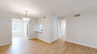 This single-story home offers a well-designed layout across four bedrooms and two bathrooms. Light wood-tone flooring flows throughout the main living areas, complemented by neutral beige walls that create a bright, clean aesthetic. The open living and dining area is anchored by a pendant light fixture and connects seamlessly to the kitchen via a pass-through counter. The kitchen is outfitted with white shaker-style cabinetry, stainless steel appliances including a dishwasher and refrigerator, a coil-top range, and a window above the sink that brings in natural light. The spacious primary bedroom features plush carpeting, a ceiling fan, and dual closets, while additional bedrooms are equally well-lit with large windows and wood-look flooring. The living room opens to an outdoor area through glass doors, allowing natural light to fill the space, and includes a ceiling fan for added comfort. Both bathrooms are finished with clean white fixtures, including a full tub-shower combination. A connecting hallway ties the layout together efficiently, making this home feel cohesive and functional throughout.