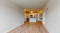 Located at 13820 S Autumn Way in Plainfield, Illinois, this single-floor residence offers a thoughtfully designed open-concept layout that seamlessly connects the living and kitchen areas. Light wood-style flooring flows throughout the space, creating a warm and cohesive aesthetic.

The kitchen is a standout feature, showcasing a two-tone design with crisp white upper cabinets and soft blue-gray lower cabinets, all complemented by clean white countertops. A central island with a double stainless steel sink serves as both a prep area and a natural gathering point. Stainless steel appliances — including a refrigerator, electric range, and over-the-range microwave — complete the contemporary look. Pendant lighting above the island and recessed ceiling fixtures add layered illumination to the space.

The open living area is generously proportioned, offering flexible arrangement potential and benefiting from natural light through a wide, multi-pane window that frames outdoor greenery. The clean, neutral walls throughout provide a versatile backdrop.

A dedicated in-unit laundry area with a stacked washer and dryer adds everyday convenience. The bathroom features a full-size soaking tub with a tiled surround and built-in corner shelving. Additional storage is available via a double-door closet in the kitchen area. The overall ambiance is bright, clean, and move-in ready.
