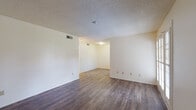 This single-story unit in Tucson, Arizona, offers a straightforward, functional layout spread across several distinct areas. The main living spaces feature dark wood-look hard-surface flooring that runs continuously, lending a cohesive feel throughout. Textured popcorn ceilings are consistent across the unit, and neutral cream-colored walls provide a clean, versatile backdrop. HVAC vents are integrated into the ceilings of the living areas, ensuring climate control throughout.

The open living and dining area is generously proportioned, with room for multiple furniture arrangements. A doorway connects these spaces to additional rooms, maintaining an accessible flow. The galley-style kitchen is lined with wood-toned lower cabinetry and white upper cabinets, complemented by light countertops, a double basin sink, and white appliances including a refrigerator and dishwasher. A window fitted with blinds allows natural light into the kitchen.

The bedrooms are carpeted in a warm, dark tone and feature neutral walls with wall-mounted lighting fixtures. One bedroom includes a window with blinds, providing natural light. The bathroom includes a full tub and shower combination with chrome fixtures and a toilet, keeping a compact and practical design.