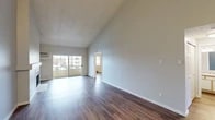 Located at 7010 N Colton St in Spokane, Washington, this single-floor unit stands out for its dramatic vaulted ceilings, which lend a sense of openness and volume well beyond what the footprint alone might suggest. Neutral gray walls and rich, dark hardwood-style flooring run throughout, creating a cohesive and clean aesthetic from room to room.

The main living area is expansive and bright, benefiting from a large sliding glass door that opens to a private balcony and allows generous natural light to fill the space. A wall-mounted air conditioning unit and baseboard heating provide year-round climate control. The textured ceiling adds a subtle architectural detail overhead.

The galley-style kitchen is efficiently laid out with white cabinetry extending to the ceiling, light-toned countertops, and white appliances including a range, dishwasher, and refrigerator. A pass-through view connects the kitchen directly to the living area.

The bedroom features vaulted ceilings, a large window with outdoor views, baseboard heating, and access to a spacious walk-in closet outfitted with multiple shelving tiers and hanging rods. The bathroom includes a wide vanity with speckled countertop, a large mirror, and globe lighting above.