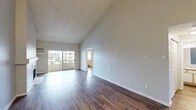 Located at 7010 N Colton St in Spokane, Washington, this single-floor unit stands out for its dramatic vaulted ceilings, which lend a sense of openness and volume well beyond what the footprint alone might suggest. Neutral gray walls and rich, dark hardwood-style flooring run throughout, creating a cohesive and clean aesthetic from room to room.

The main living area is expansive and bright, benefiting from a large sliding glass door that opens to a private balcony and allows generous natural light to fill the space. A wall-mounted air conditioning unit and baseboard heating provide year-round climate control. The textured ceiling adds a subtle architectural detail overhead.

The galley-style kitchen is efficiently laid out with white cabinetry extending to the ceiling, light-toned countertops, and white appliances including a range, dishwasher, and refrigerator. A pass-through view connects the kitchen directly to the living area.

The bedroom features vaulted ceilings, a large window with outdoor views, baseboard heating, and access to a spacious walk-in closet outfitted with multiple shelving tiers and hanging rods. The bathroom includes a wide vanity with speckled countertop, a large mirror, and globe lighting above.