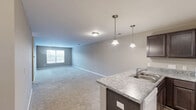 Located at 1034 Finnwood Dr in Whitsett, NC, this single-story, 3-bedroom, 2-bathroom home offers a well-organized and functional floor plan. The open-concept living area seamlessly connects the kitchen, dining, and living spaces, creating a bright and cohesive environment. The kitchen is a standout feature, equipped with dark espresso cabinetry, granite-style laminate countertops, a peninsula with a built-in sink, pendant lighting, a track lighting system, and white appliances including a refrigerator, range, and over-the-range microwave. Wood-look flooring anchors the kitchen, while plush carpeting flows through the living area and all bedrooms. The spacious primary bedroom includes a ceiling fan with light fixture and a closet, while the two additional bedrooms each feature natural light from large windows and dedicated closet space. The bathrooms are finished with dark wood vanities, neutral countertops, and tiled shower surrounds. Additional highlights include a dedicated laundry room, a pantry, and four closets throughout the home. Neutral warm-toned walls and consistent finishes give the home a clean, move-in-ready appeal.
