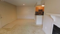 Located at 710 Lindh Rd in Gulfport, Mississippi, this single-story space offers a comfortable and functional layout with a warm, understated aesthetic throughout. The living area is generously proportioned, featuring plush carpeting, a ceiling fan with integrated lighting, and a classic white-manteled fireplace that serves as a natural focal point. A large sliding glass door floods the room with abundant natural light, framed by vertical blinds for privacy and light control. The textured ceiling adds subtle character to the space. Adjacent to the living area, the kitchen is accessible through an open pass-through design, creating a connected and airy feel. It features warm honey-toned wood cabinetry, a striking dark mosaic tile backsplash, and dark countertops that provide a bold contrast. A dedicated sink area adds practicality, and recessed and flush-mount lighting keeps the kitchen bright and functional. The transition between the carpeted living space and the tile flooring in the kitchen area is clean and well-defined, highlighting the thoughtful zoning of the layout. Overall, the space presents a neutral palette throughout, offering a versatile and move-in ready environment in a convenient Gulfport location.