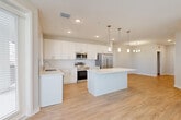Located at 1387 East Vine Street in Kissimmee, FL, this well-appointed single-story home offers three bedrooms, two bathrooms, and a thoughtfully designed open-concept layout. The heart of the home is a bright, combined living, dining, and kitchen area featuring warm wood-look flooring, recessed lighting, and elegant pendant fixtures. The modern kitchen is outfitted with crisp white shaker cabinetry, a geometric hexagon-tile backsplash, light quartz countertops, a central island, and a full suite of stainless steel appliances including a range, microwave, dishwasher, and refrigerator. The living area benefits from a bank of large windows and a ceiling fan, allowing generous natural light and outdoor views. The bedrooms are carpeted for comfort, with the spacious primary bedroom featuring a walk-in closet with wire shelving systems. Both bathrooms are finished with marble-look porcelain tile flooring and surround, with one offering a soaking tub and shower combination and the other a glass-enclosed walk-in shower with brushed gold fixtures and a white vanity. Additional spaces include a bonus room, laundry area, utility room, and multiple closets for ample storage throughout.